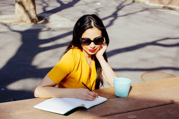 Portrait of a smiling woman with sunglasses writing in a notebook and looking down in the park