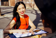 Portrait Of A Young Brunette Woman With Workbook Smiling At Another Person In The Park
