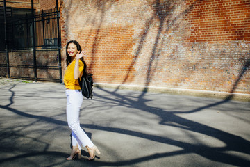 Wall Mural - Portrait of a young woman with backpack walking in front of a brick building, waving at camera