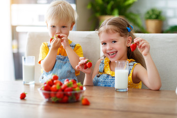 Happy children brother and sister eating strawberries with milk