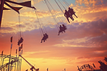 people riding rides and enjoying the summer atmosphere at a state fair at dusk toned with a retro vintage filter app or action