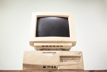 Front side of old and obsolete computer on old wood table with coloured concrete wall background