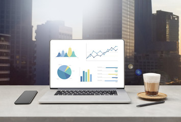Poster - laptop showing blank screen with cup of coffee and mobile phone on table against beautiful business modern office buildings background. technology concept 