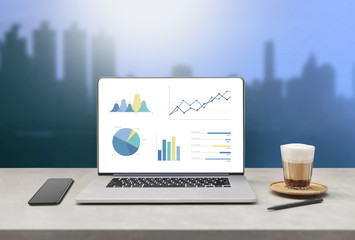 Poster - laptop showing blank screen with cup of coffee and mobile phone on table against beautiful business modern office buildings background. technology concept 