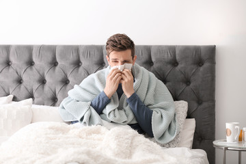 Wall Mural - Sick young man with tissue suffering from cold in bed