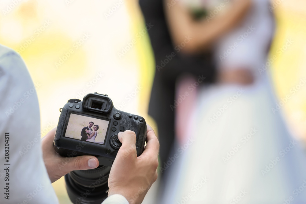 Professional photographer with camera and wedding couple, outdoors - obrazy, fototapety, plakaty 