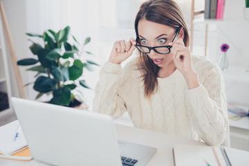 Portrait of stressed unexpected shocked woman looking out glasses on her face at screen of computer holding eyelets with hands having big eyes sitting on work place station