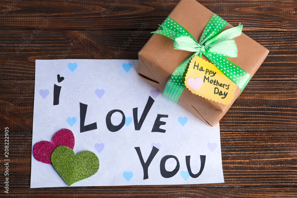 Composition with gift and card on wooden background. Greetings for Mother's Day