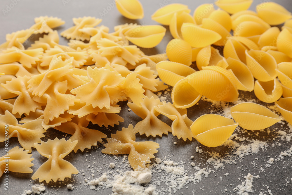 Different uncooked pasta and flour on grey background
