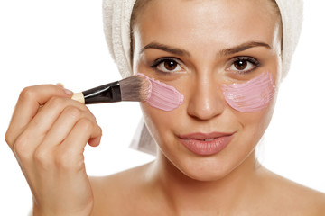 young beautiful woman applyong facial mask on her face with a towel on her head