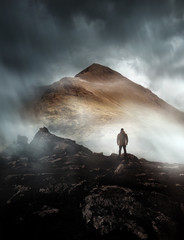 Wall Mural - a person hiking looks onwards at a mountain shrouded in mist and clouds with the peak visible. sceni