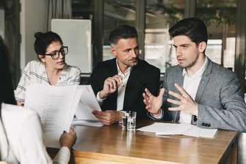 Poster - Group of business people in formal suits sitting at table in office, and talking with young woman about work during job interview - business, career and placement concept