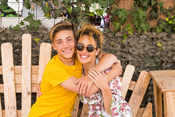 mother and son hugging with smile and enjoy leisure time together with love. family teenager boy 14 years old and mom 43 have fun sitting on a wodd bench outdoor in a sunny day. happiness family