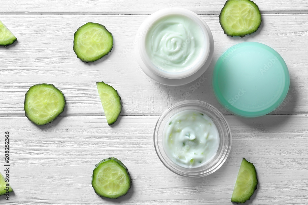 Composition with body cream and cucumber slices on white wooden background