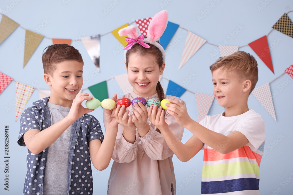 Cute little children with Easter eggs near decorated wall
