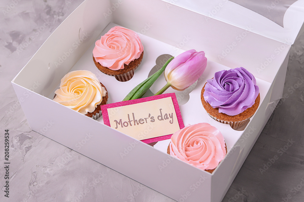 Box with tasty cupcakes and tulip on grey background. Mother's day celebration