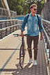 © Fxquadro - Handsome hipster with a stylish haircut in sunglasses walking with bicycle outdoors.