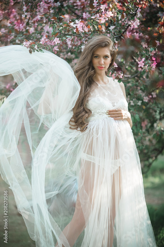 Pregnant pretty woman is wearing white fashion dress posing in pink blossom appl Poster