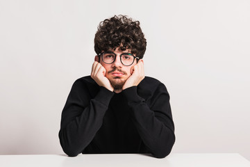 Wall Mural - Young bored man in a studio, sitting at the table.