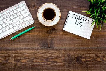Poster - Template for contacts, background for contact information. Lettering Contact us in notebook on office work desk with computer on dark wooden background top view space for text