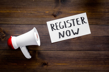 Poster - Register now hand lettering icon near megaphone on dark wooden background top view copy space