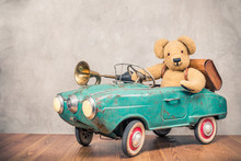 Teddy Bear And Old Leather School Bag Driving In Rusty Retro Turquoise Toy Pedal Car With Classic Brass Klaxon In Front Concrete Textured Wall Background. Vintage Style Filtered Photo