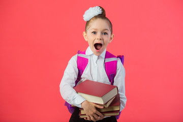 Wall Mural - beautiful little girl with a bow with a school satchel on a pink background with a book in hands