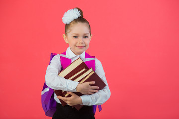 Wall Mural - beautiful little girl with a bow with a school satchel on a pink background with a book in hands