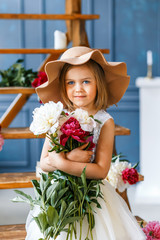 Cute little girl in fashionable hat with peonies in studio