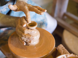 Rotating potter's wheel and clay ware on it vase: taken from above. Hands in clay. Pottery: male ceramist creates a hand made clay product. Process of rotation of potter's wheel, hands of ceramist.