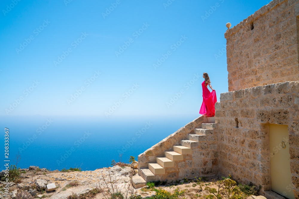 Sexy girl in a long pink dress walking down the ocean on the top of the ...