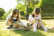 © Valerii Honcharuk - Two little girl friends schoolgirl learns sitting on a meadow in the park. Children with backpacks, books, notebooks.