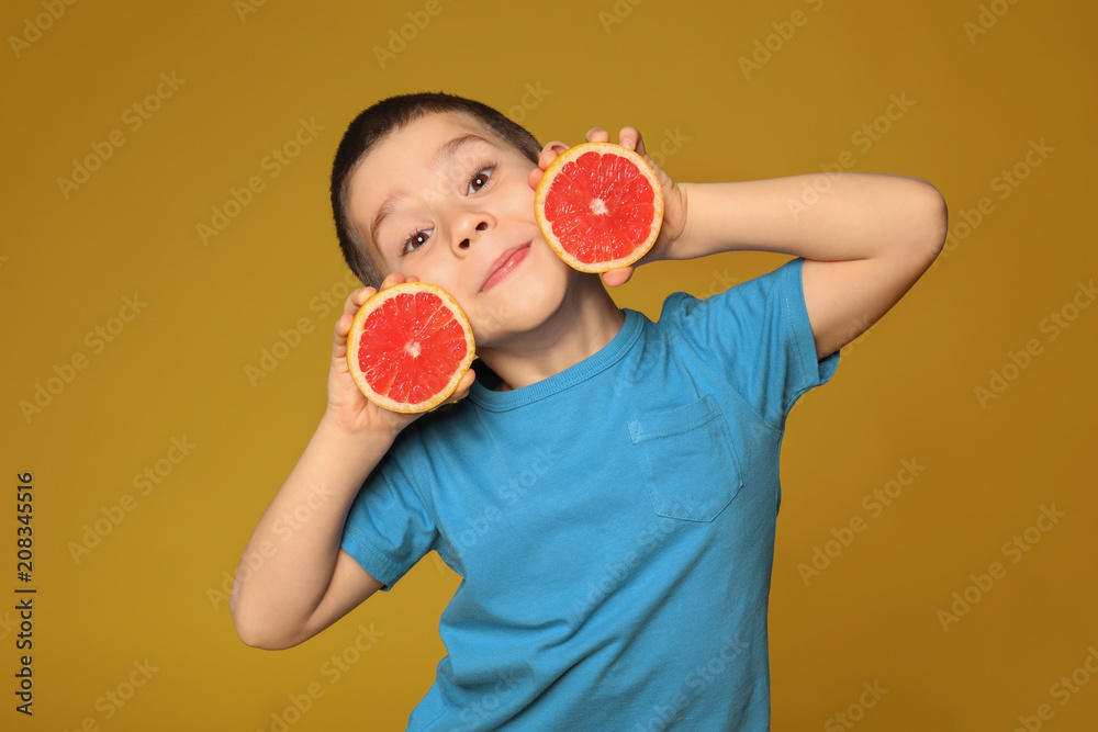 Funny little boy with citrus fruit on color background