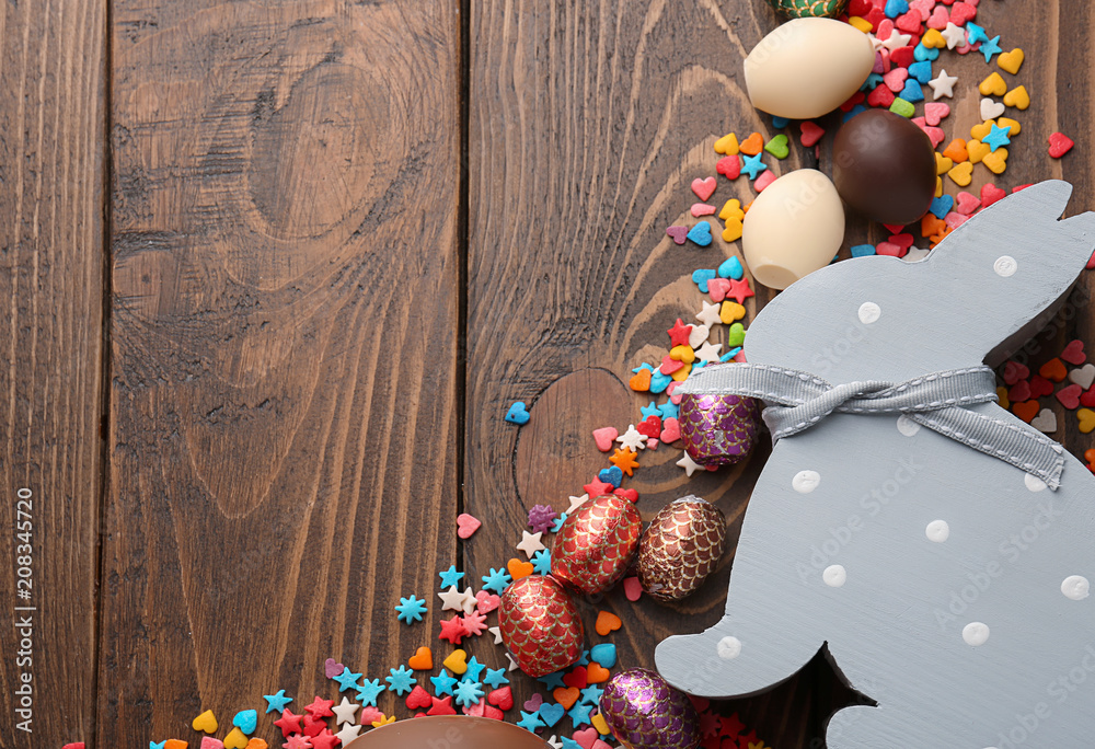 Composition with chocolate Easter eggs, colorful sprinkles and bunny toy on wooden background