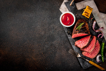 Wall Mural - Fresh grilled beef, homemade bbq meat medium rare, on black stone cutting board, with spices, dark background, copy space above