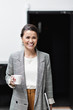 © Maskot - Portrait of smiling businesswoman looking away while holding coffee cup at office