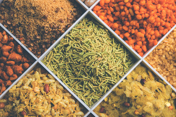 Indian Tea-time snacks like sev, chivda, farsan, mixture, boondi, bakarwadi etc served in white wooden box with cells. selective focus