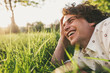 © iuricazac - Horizontal close up portrait of happy young male with curly hair, smiling and relaxing on the green grass in the park, looking at the nature. Copy space for advertising. People and lifestyle concept.