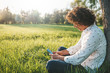 © Z A C - Stylish male with curly hair sitting outdoors in the park checking his news feed or messaging via social networks using smart phone using free wireless. Happy student receiving pleasant news on mobile