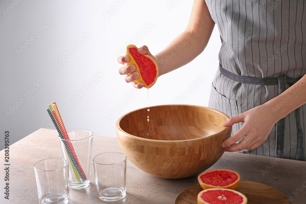 Woman squeezing citrus fruit over bowl on table