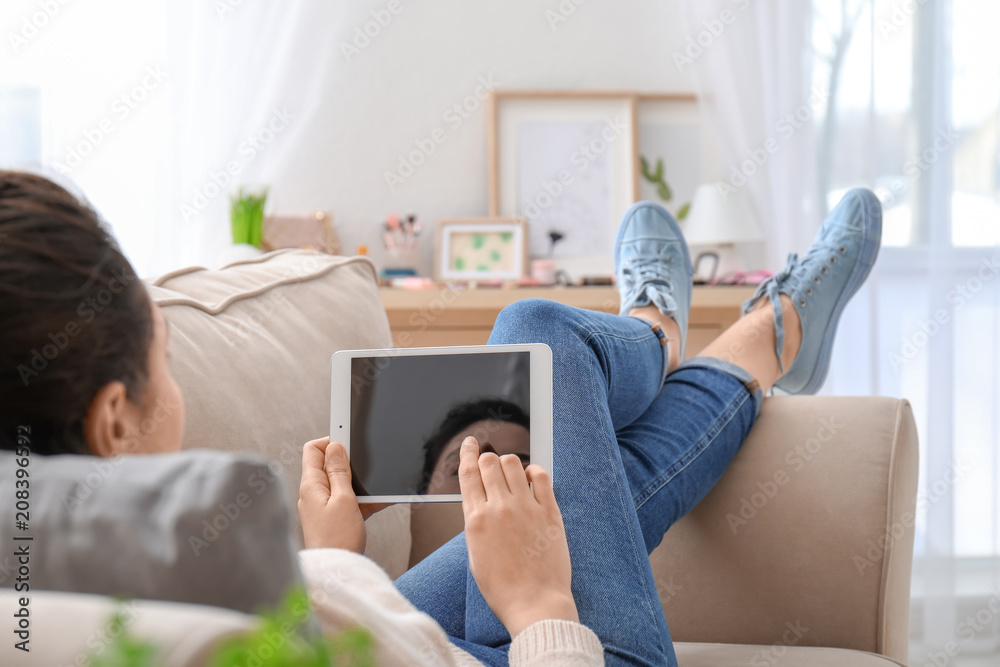 Young woman using tablet computer while resting on couch at home