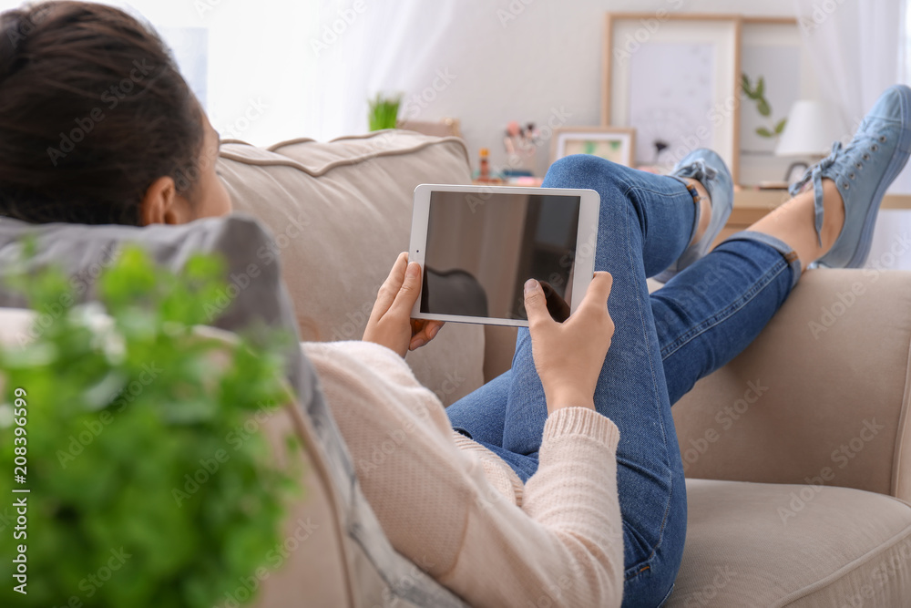 Young woman using tablet computer while resting on couch at home