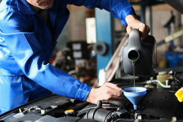 male mechanic refilling car oil in service center