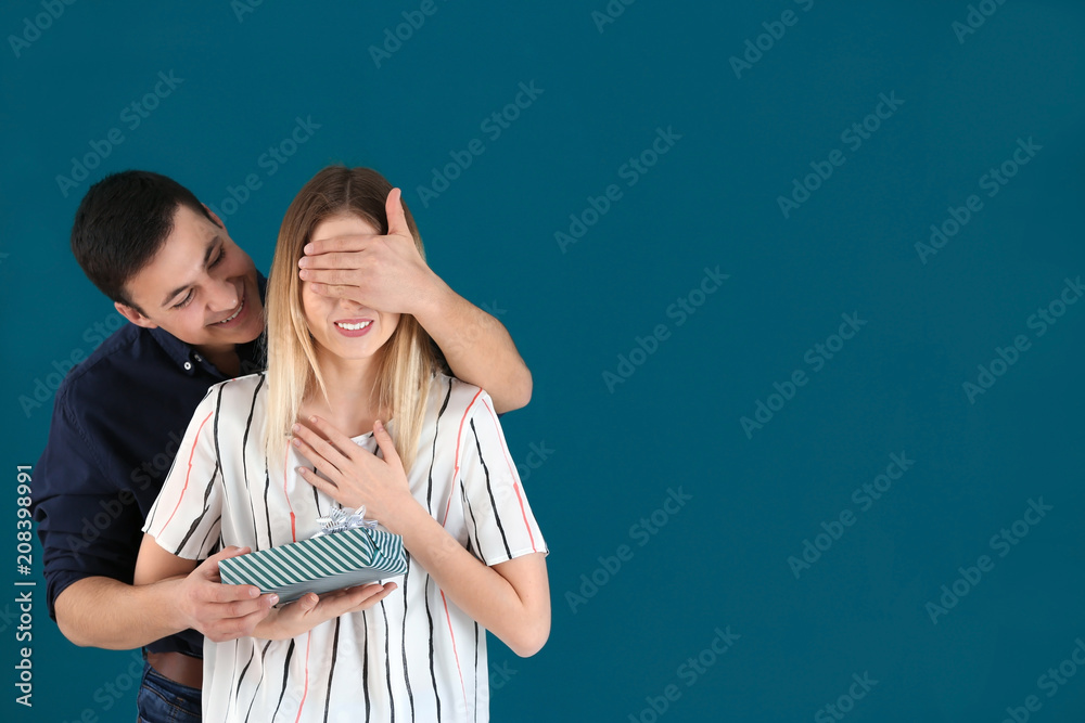 Young man giving present to his beloved girlfriend on color background