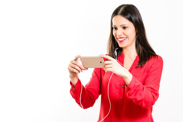 Young brunette with red clothes holding smartphone with hands horizontally, displaying the phone screen, enjoying music and video - isolated on white background