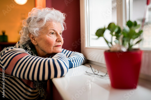 Cuadros en Lienzo Sad alone senior woman looking through window