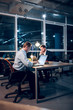 © Svyatoslav Lypynskyy - Couple of colleagues sitting at office table with laptops. Two serious businessmen working in middle of night in their modern office with glass windows.