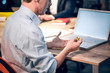 © Svyatoslav Lypynskyy - Senior man sitting in front of computer with bitcoin. Cropped picture of guy wearing blue shirt holding golden coin in his hands while sitting at wooden table with laptop on it.