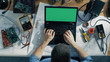 © Gorodenkoff - Top View of a Gifted IT Technician Types on His Green Screen Laptop while Sitting at His Desk, He's Surrounded By Various Technical Components, Drafts. Sun Shines on His Desk.