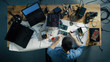 © Gorodenkoff - Top View of Young IT Technician Soldering Circuit Board. His Table is Full With Various Computer Parts, Motherboards, Laptops, Cables. Morning Sun Illuminates His Desk.